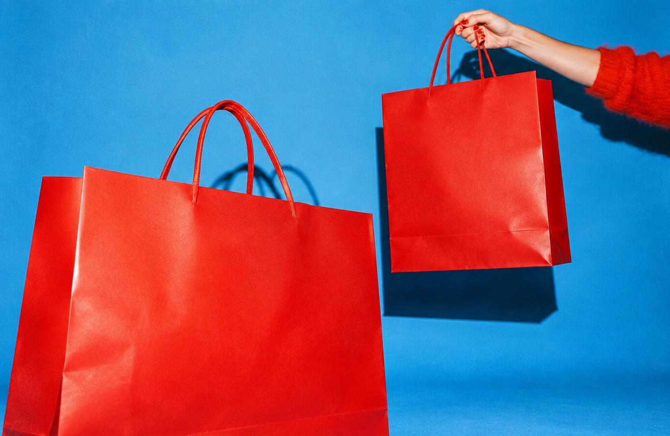 Hand holding a bright red shopping bag with a second oversized bag against a blue backdrop